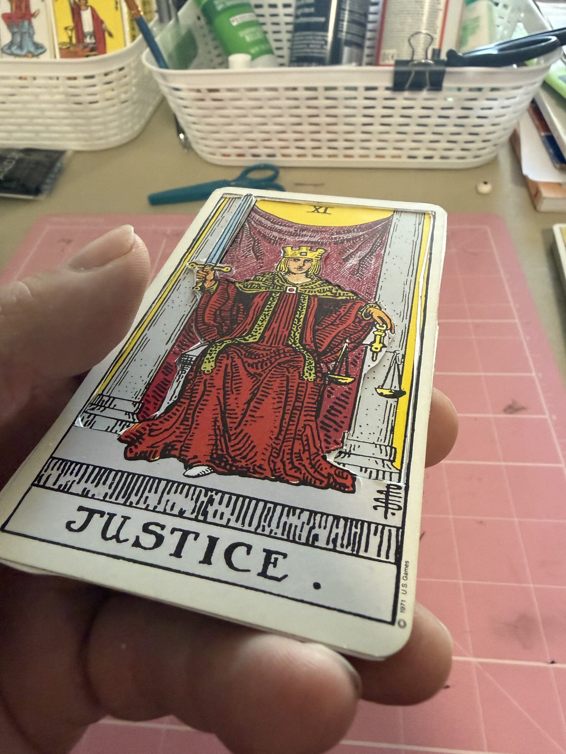 Hand holding Justice tarot card with detailed handcrafted design and workspace background